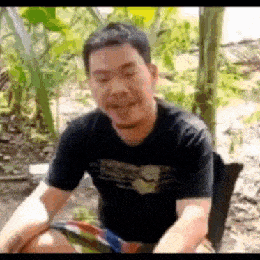 a man in a black shirt is sitting on a chair in the woods and smiling .