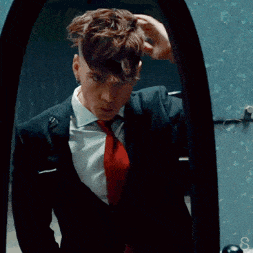 a man in a suit and tie covering his face in front of a mirror