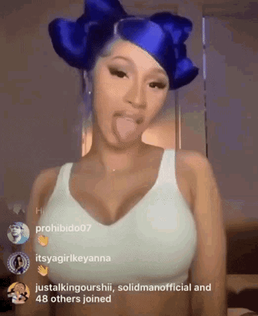 a woman with blue hair is sticking her tongue out in front of a bunch of people