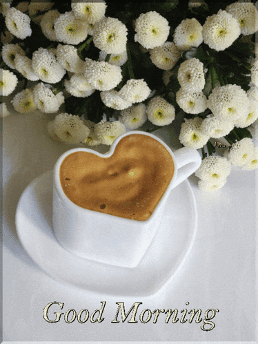 a cup of coffee in the shape of a heart on a saucer with flowers in the background