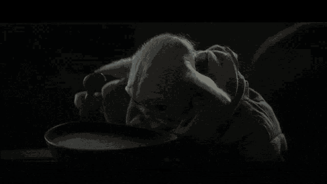 a baby yoda is eating from a bowl with a spoon in it .