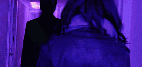 a person in a hood is standing in front of a purple light .