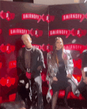 a man and a woman are dancing in front of a smirnoff wall