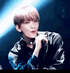 a young man wearing a choker and a black jacket is sitting on a stage .