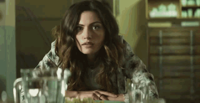 a woman is sitting at a table with her hands on her hips and looking at the camera .