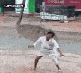 a man in a white shirt and shorts is standing on a muddy street .