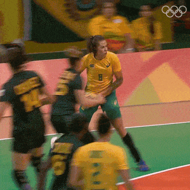 a woman in a yellow shirt with the number 8 on it stands in front of a group of players