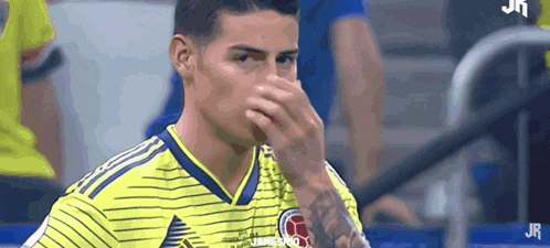 a soccer player covering his nose with his hand while wearing a yellow and blue striped jersey