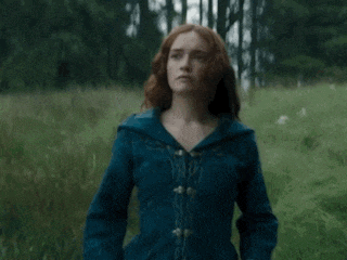 a woman with red hair is standing in a field looking at something .