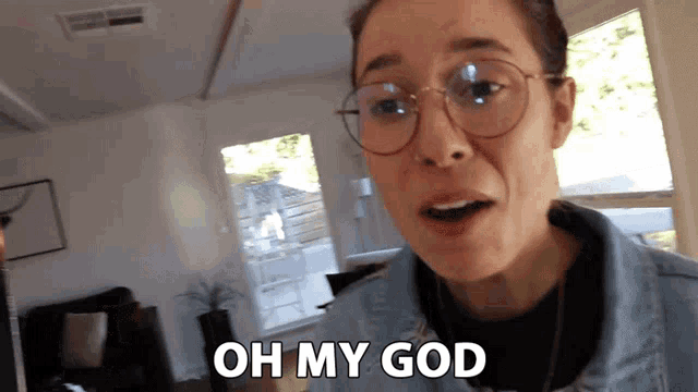 a woman wearing glasses and a denim jacket is saying oh my god