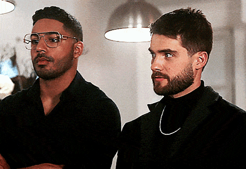 two men standing next to each other one wearing glasses and the other a turtleneck