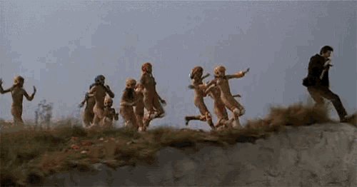 a group of people are running down a hill with a man in a suit in the background