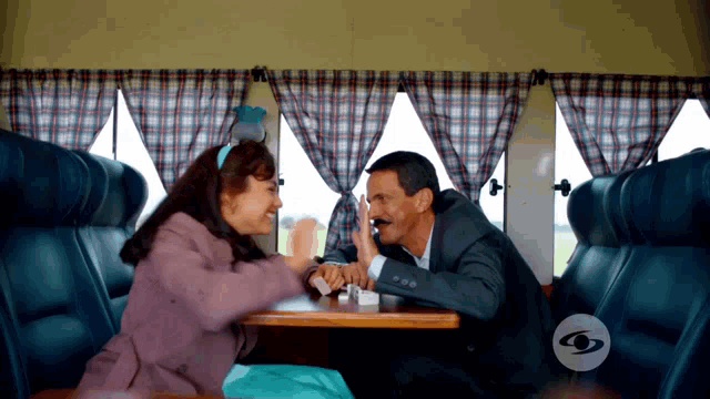 a man and a woman are sitting at a table in front of a sign that says tv