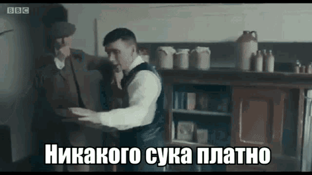 a man in a suit is standing next to another man in a kitchen and holding a plate .
