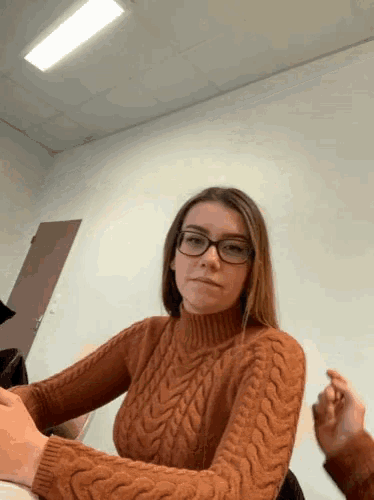 a woman wearing glasses and a sweater sits at a table