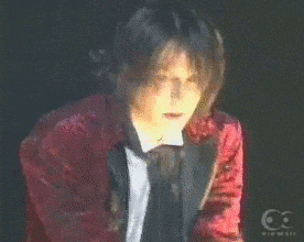a man in a red jacket and black tie is looking at the camera .