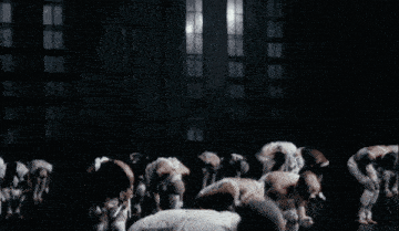 a woman in a white outfit with a cross on her chest is dancing in front of a group of people