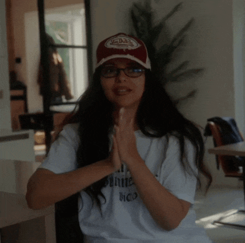 a woman wearing glasses and a von dutch hat holds her hands together