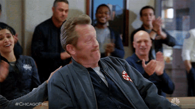 a man in a chicago fire jacket is sitting in front of a group of people clapping