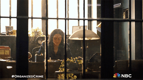 a woman sits at a desk in a jail cell with the nbc logo on the bottom
