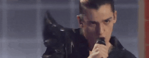 a man is singing into a microphone while wearing a black leather jacket .