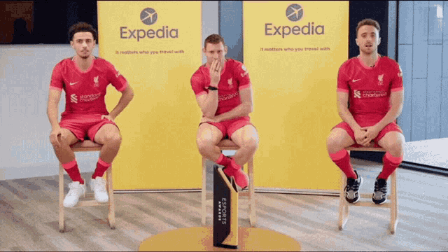 three soccer players sitting in front of a expedia sign