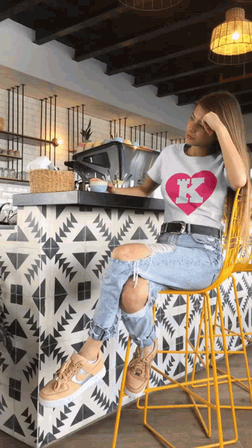 a woman wearing a white shirt with the letter k on it sits in a yellow chair