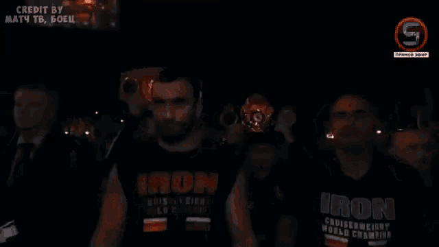 a man wearing a black shirt that says iron is walking in a dark room
