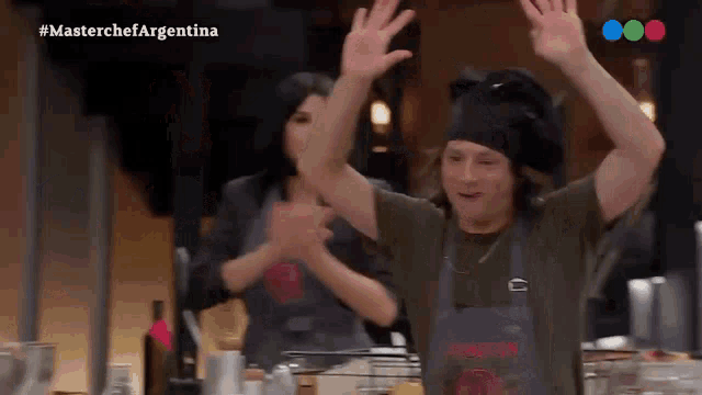a man in a chef 's hat is raising his hands in the air while a woman looks on