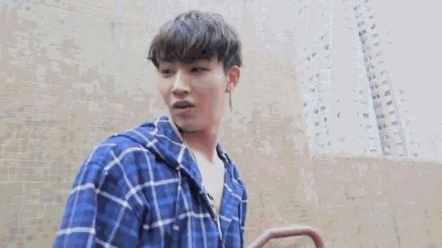 a young man in a blue plaid shirt is standing in front of a brick wall .