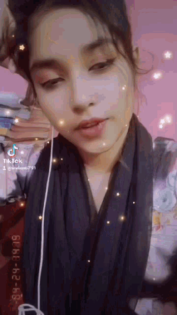a woman wearing headphones and a scarf is taking a selfie with a pink background .