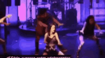 a group of people are dancing on a stage in front of a purple background