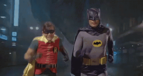 batman and robin are running down a street together