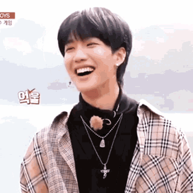 a young man wearing a plaid shirt and a black turtleneck is laughing .