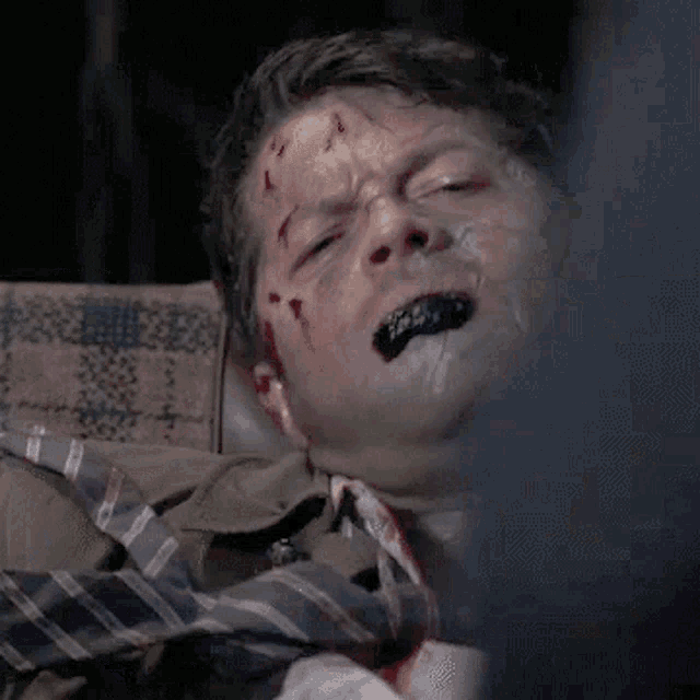 a man with blood on his face is laying in a chair with a tie .