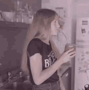 a woman drinking from a glass with a straw wearing a black shirt that says billa