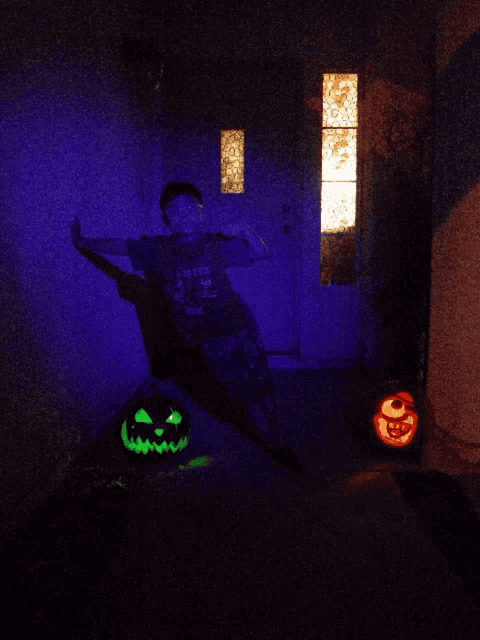 a boy in a green shirt with the word abc on it stands in front of a glowing pumpkin