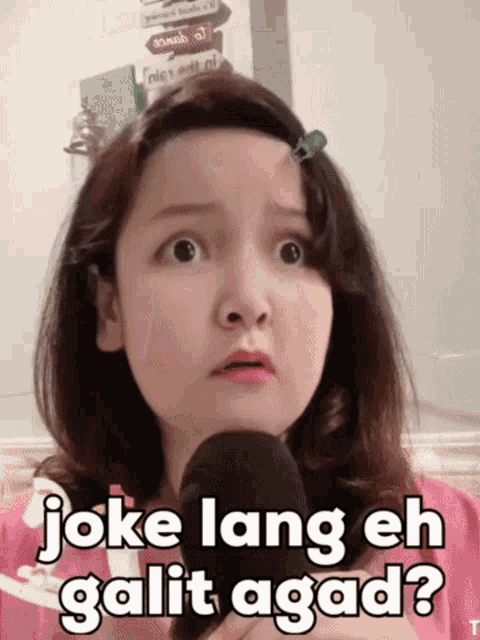 a little girl is holding a microphone with the words joke lang eh galit agad written on it