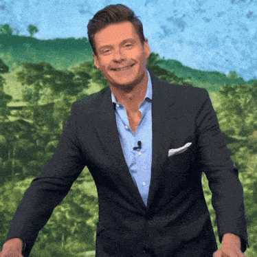 a man in a suit and blue shirt is smiling in front of a green background