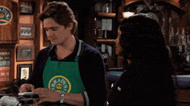 a man wearing a green apron that says ' no smoking ' on it talks to a woman