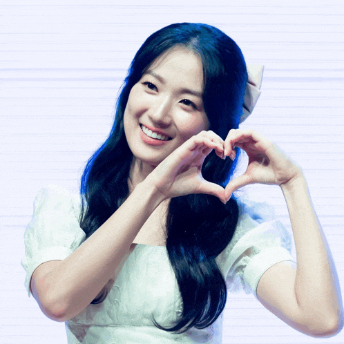 a woman in a white dress making a heart with her hands