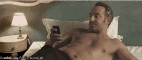 a shirtless man laying on a bed looking at his phone