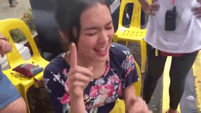 a woman in a floral shirt is giving a thumbs up while sitting in a chair .