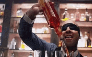 a man wearing blindfolds is pouring a drink from a bottle into a glass .