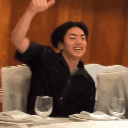 a man sitting at a table with his arm in the air and a glass of wine