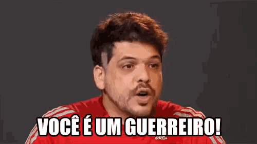 a man with a beard and mustache is wearing a red shirt and saying voce e um guerreiro !