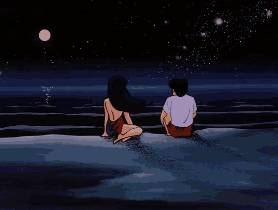 a man and a woman are sitting on the beach at night