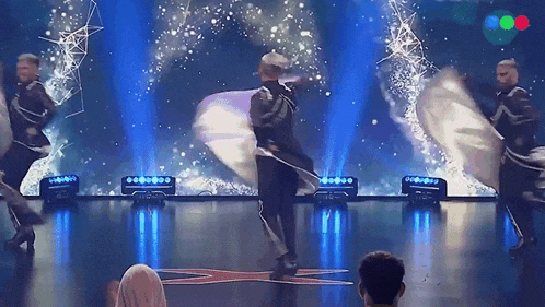 a group of people are dancing on a stage in front of a blue light