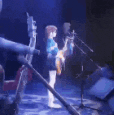 a person is playing a guitar on a stage while another person stands behind them .