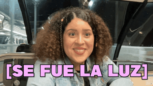 a woman with curly hair is smiling in front of a sign that says ' se fue la luz '
